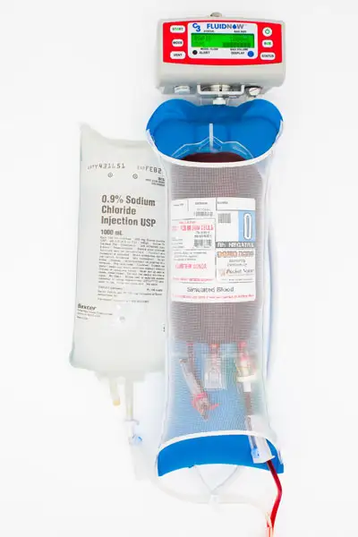 FluidNow rapid volume infuser connected to a saline bag and a simulated blood bag, laid flat on a white surface for emergency or trauma setup.